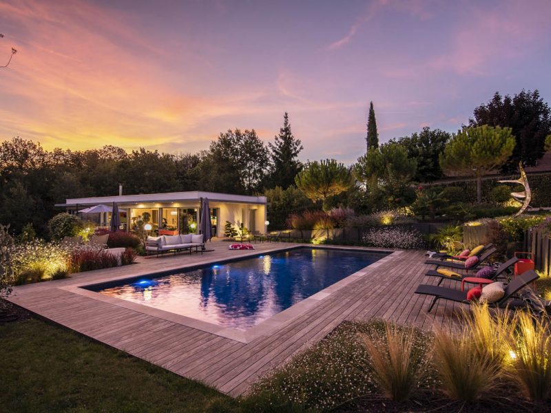 piscine vue de nuit avec terrasse en bois et éclairage dans les massifs