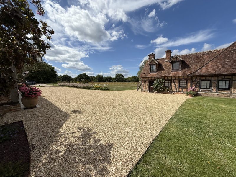 Grande cour gravillonnée devant maison à colombages avec vue sur parc paysager